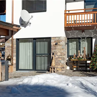 A modern house with a snow-covered garden. In front of the house stands a Christmas tree and festive decorations.
