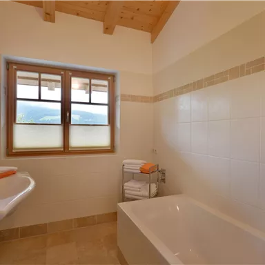 A modern bathroom with a bathtub and a sink. Large windows provide plenty of daylight.