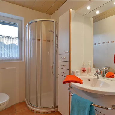 A modern bathroom with a shower, a sink, and light-colored walls. Towels in orange and blue are decorated on the walls.
