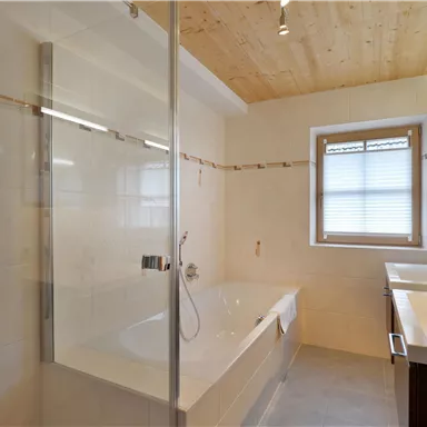 Ein modernes Badezimmer mit einer Badewanne und einer separaten Dusche. Große Fenster sorgen für viel Tageslicht.