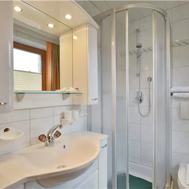 Ein modernes Badezimmer mit einer Dusche und einem Waschbecken. Die Wände sind gefliest, und es gibt große Fenster für natürliches Licht.