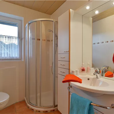 A modern bathroom with a shower, a sink, and light-colored walls. Towels in orange and blue are decorated on the walls.