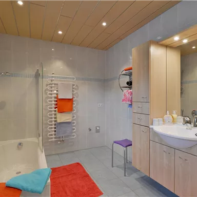 A bright bathroom with a bathtub and a modern sink. Colorful towels and a chair add coziness.