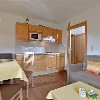 A cozy apartment with a wooden kitchen, a dining table, and a comfortable seating area. The room is bright and friendly designed.