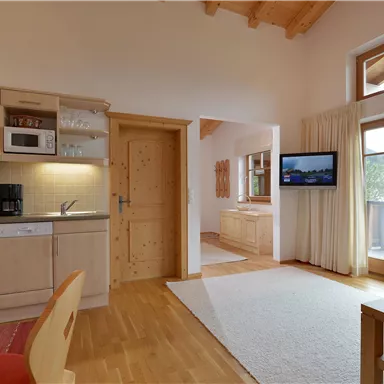 A cozy living space with a modern kitchen and large windows. Bright furniture creates an inviting atmosphere.