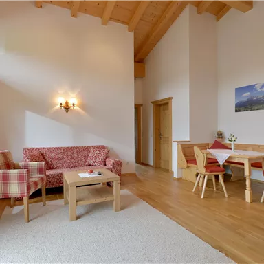 A cozy living space with high ceilings and wooden details. It has a seating area with a sofa and a dining table with chairs.