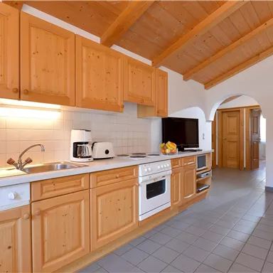 A modern kitchen with wooden cabinets and a bright, open space. In the corner, there is a cozy armchair and the furnishings are functional.