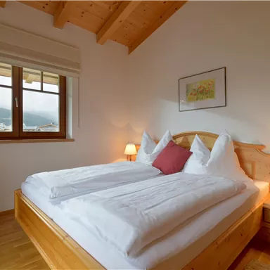 A cozy bedroom with a double bed and a warm wooden ceiling. The room has a window with a view of the landscape and a pleasant lighting.