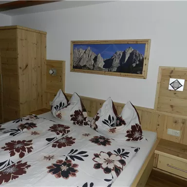 Ein gemütliches Schlafzimmer mit einem Doppelbett und dekorativen Kissen. Die Wände sind aus Holz, und ein Bild mit Bergen schmückt die Wand über dem Bett.