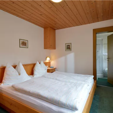 Ein gemütliches Schlafzimmer mit zwei Betten und Holzmöbeln. Der Raum hat eine warme Atmosphäre und einen Blick auf ein angrenzendes Bad.
