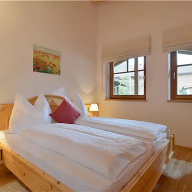 A cozy bedroom with a double bed and wooden paneled walls. The windows let in plenty of daylight, creating an inviting atmosphere.