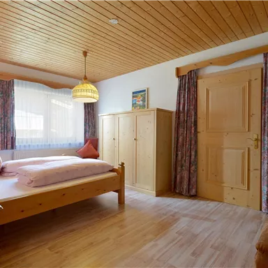 A cozy bedroom with a wooden bed and a corner to relax. Large windows bring in lots of light, and the decor is simple and stylish.