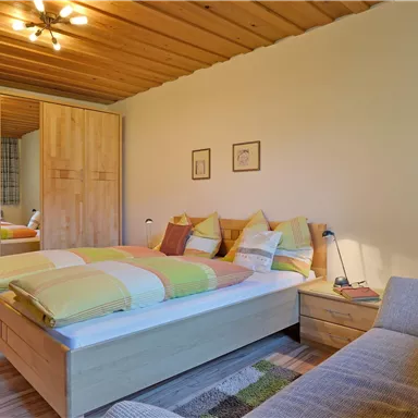 Ein gemütliches Schlafzimmer mit einem großen Bett und bunten Kissen. Der Raum hat Holzdetails und große Fenster, die viel Licht hereinlassen.
