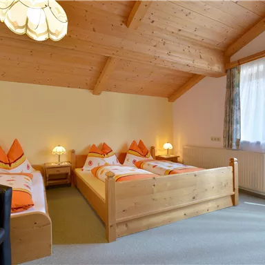 A cozy bedroom with three wooden beds and a warm wooden ceiling. The windows let in plenty of light and create a pleasant atmosphere.