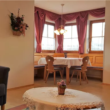A cozy living area with a gray sofa and a round table. The room has large windows with curtains and an inviting seating corner.