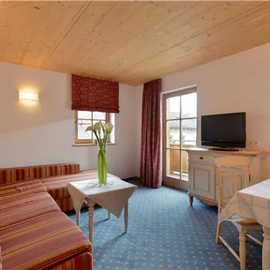 Ein gemütliches Wohnzimmer mit einem Sofa und einem Tisch. Es gibt einen Fernseher und einen Zugang zu einem Balkon.