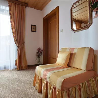 A cozy area with an upholstered armchair and a large window. The room is bright and friendly with a warm tone.
