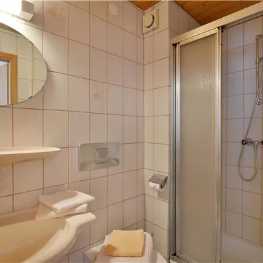 A modern bathroom with a shower and a sink. The walls are tiled in light colors and there is a round mirror.