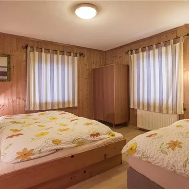 Ein gemütliches Schlafzimmer mit Holzvertäfelung und zwei Betten. Die Wände sind mit passenden Vorhängen und einem Spiegel dekoriert.