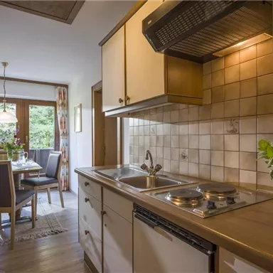 A bright kitchen with modern appliances and wooden surfaces. In the background, there is a dining area with a view of the outdoors.