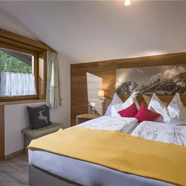 A comfortable bedroom with a large bed and colorful pillows. Large windows let in daylight and provide a view of nature.