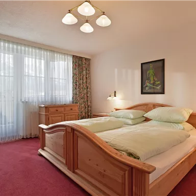 Ein gemütliches Schlafzimmer mit einem Doppelbett und zwei Nachttischen. Große Fenster sorgen für viel Tageslicht und eine warme Atmosphäre.