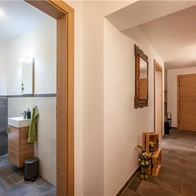 Ein heller Flur mit Holzverkleidungen und modernen Badezimmer. Rechts führen Türen zu weiteren Räumen, die eine einladende Atmosphäre schaffen.