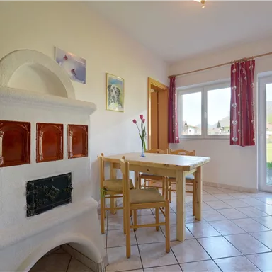 A cozy kitchen with a table and chairs. A traditional fireplace and large windows provide plenty of light.