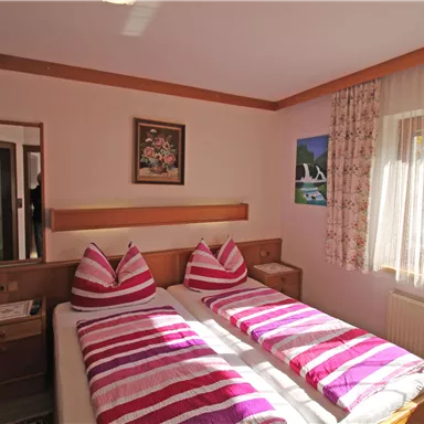 A cozy bedroom with two single beds and colorful striped bed covers. Large windows provide plenty of daylight and a pleasant atmosphere.
