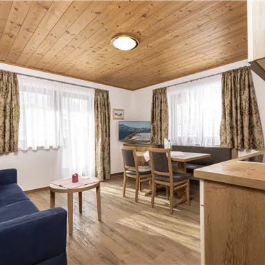 A cozy living space with a blue couch and a wooden table. Large windows provide plenty of daylight and an inviting atmosphere.