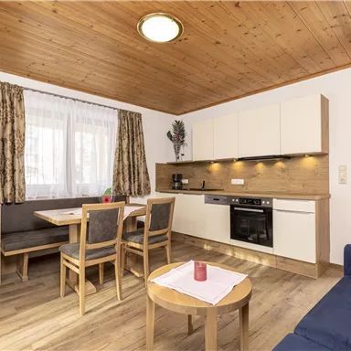 A cozy living kitchen with wooden ceilings and modern furniture. The space is bright and inviting, featuring a dining table and a seating area.