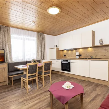 A modern kitchen with wooden decor and a dining area. The room has a television, bright curtains, and a cozy atmosphere.