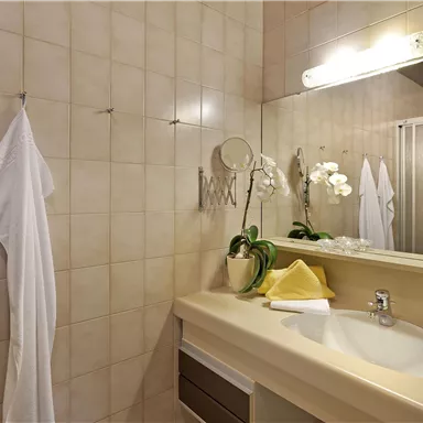 Ein modernes Badezimmer mit hellem Fliesenboden und einem Waschbecken. Handtücher und eine Pflanze verleihen dem Raum eine einladende Atmosphäre.