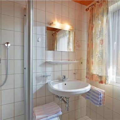 Ein helles Badezimmer mit Dusche, Waschbecken und Fenster. Die Wände sind gefliest und es gibt mehrere Handtücher.