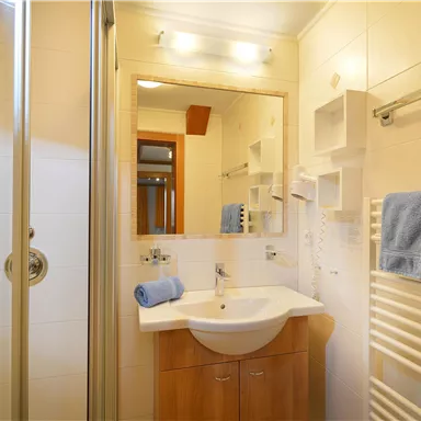 A bright bathroom with a shower and sink. Towels and a mirror are also available.