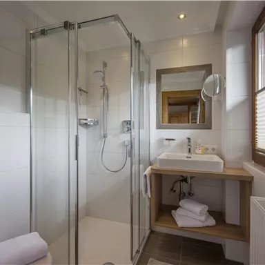 A modern bathroom with a glass shower and a wooden sink. The windows let in plenty of daylight.
