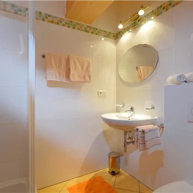 A modern bathroom with a shower, a sink, and a large mirror. The walls are brightly tiled and the ambiance feels clean and inviting.