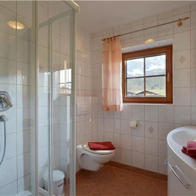 A modern bathroom with a shower, a toilet, and a washbasin.
Large windows let in plenty of light, and the towels are in red.