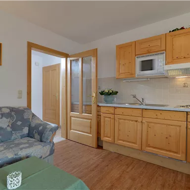 A cozy kitchen-living room with wooden cabinets and modern appliances. The space is bright and inviting, with a sofa and a table.
