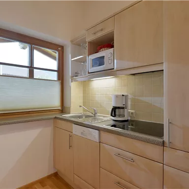 A bright kitchen with wooden cabinets and modern appliances. A window provides natural light and a friendly atmosphere.