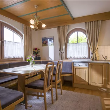 A cozy kitchen with wooden furniture and a dining area. Large windows let in plenty of light and create an inviting atmosphere.