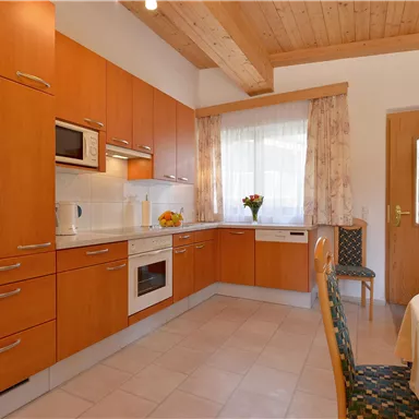 A modern kitchen with wooden cabinets and bright walls. There is a table with chairs and fresh flowers on the countertop.