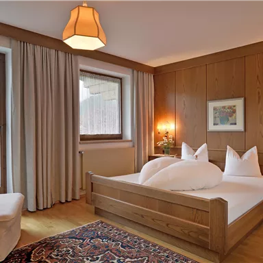 Ein gemütliches Schlafzimmer mit Holzwänden und einem großen Fenster. Das Bett ist mit weißen Kissen und Decken ausgestattet, und ein Teppich liegt auf dem Boden.