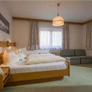 A cozy bedroom with two beds and a sofa. The windows let in plenty of light and the decor is simple and modern.