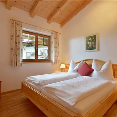 A cozy bedroom with two beds and wooden fittings. There is a window with a view outside and pleasant lighting.