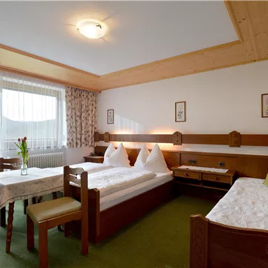 Ein gemütliches Hotelzimmer mit zwei Betten und einem Tisch. Große Fenster lassen viel Licht herein und der Platz ist mit natürlichen Materialien dekoriert.