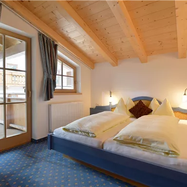 Ein gemütliches Schlafzimmer mit Holzdecken und einem großen Doppelbett. Der Raum verfügt über einen Balkon mit Blick nach draußen.