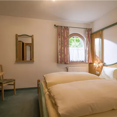 A cozy bedroom with a large bed and a table. The windows let in plenty of natural light and the walls are bright and cheerful.