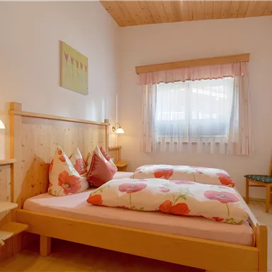 A cozy bedroom with two beds and bright colors. Large windows provide plenty of daylight and an inviting atmosphere.