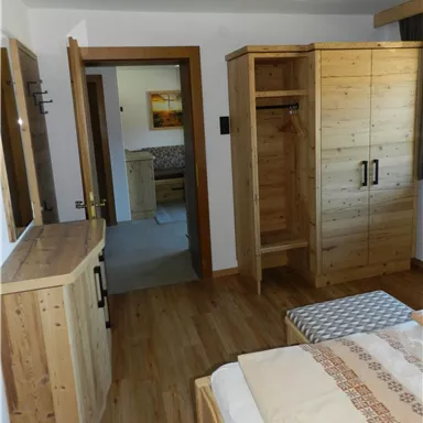 Ein gemütliches Schlafzimmer mit Holzmöbeln und einem großen Fenster. Der Raum ist hell und einladend, mit einem Blick auf einen angrenzenden Raum.